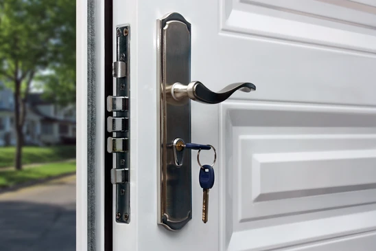 Extérieur résidentiel avec porte d'entrée blanche ouverte, poignée métallique actionnée, clés suspendues dans la serrure