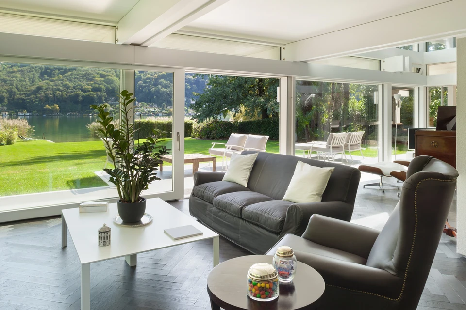 Salon moderne avec baies vitrées panoramiques donnant sur jardin et lac