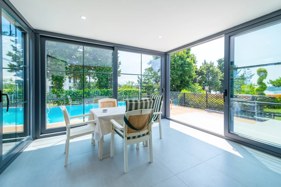 Salon moderne avec canapés gris modulaires disposés face à une grande baie vitrée coulissante donnant sur terrasse et jardin arboré